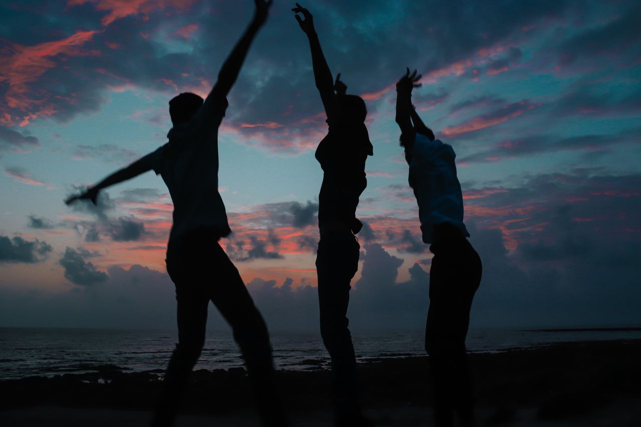 silhouettes of three people dancing joyfully against a vibrant beach s