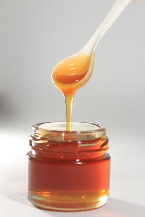 Free Vibrant close-up of golden honey drizzling from spoon into jar, showcasing its sticky texture. Stock Photo
