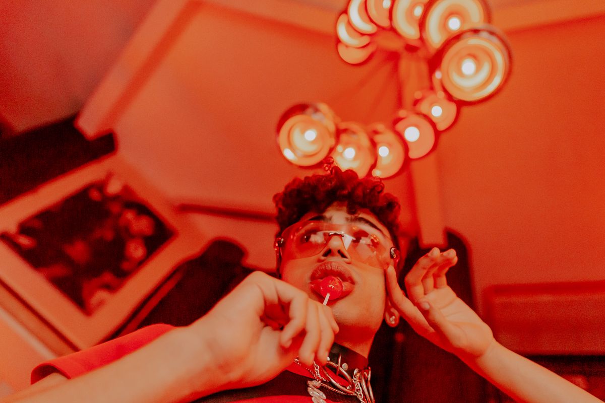 Stylish man enjoying a lollipop under vibrant red lighting indoors.
