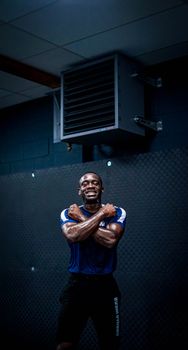 A fit African American man poses confidently with arms crossed in a gym setting, wearing sportswear.