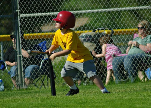 A Young Boy in Yellow Shirt Wearing a Red Batting Helmet while Playing Baseball