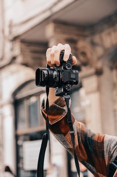Hand holding a modern camera in a city setting, capturing urban life.