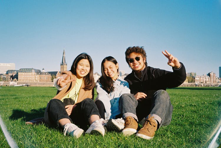 Happy Teenagers Sitting On Grass Field