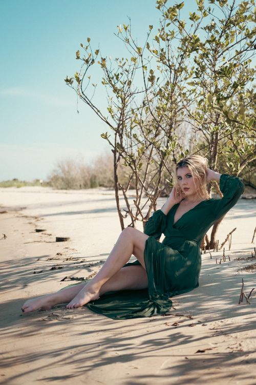 Free Striking portrait of a woman in a green dress posing on a sandy, sunny beach. Stock Photo