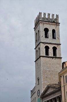 The Torre del Popolo stands tall in Assisi, showcasing its ancient gothic architecture under a cloudy sky.