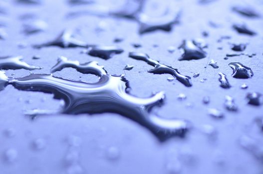 Close-up image of water droplets scattered on a reflective surface with a cool tone.