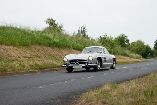 Vintage Mercedes Benz sports car driving on country road with lush greenery.