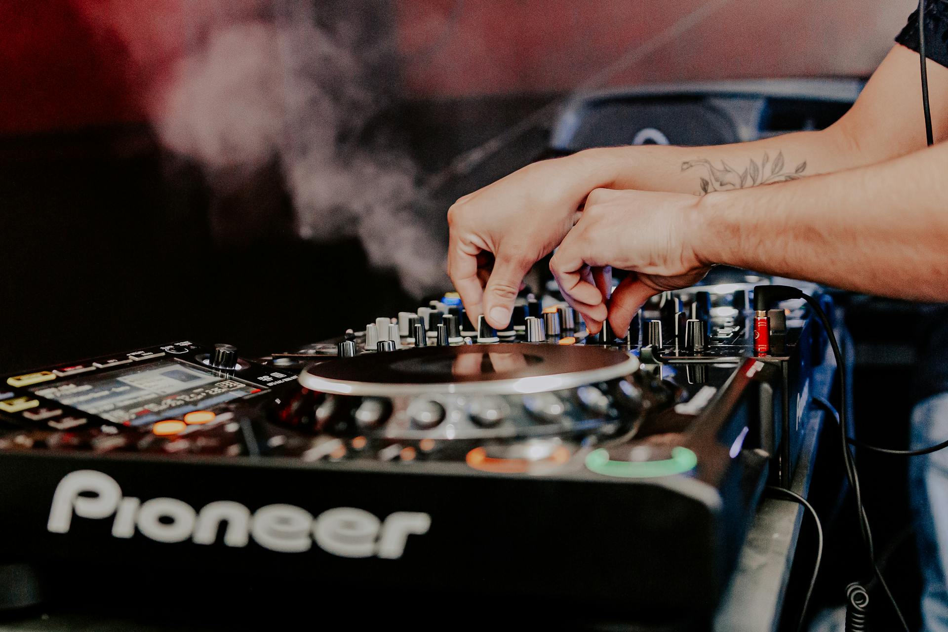 Hands of a DJ operating a Pioneer mixer with smoke at a São Paulo club.