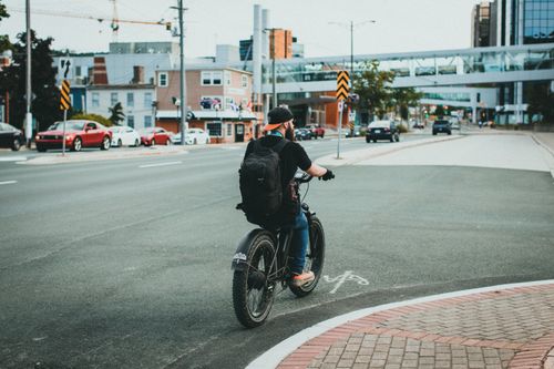 Free Man riding a bicycle on a city street while wearing a backpack, urban life. Stock Photo