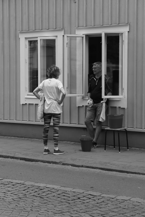 Free Black and white photo of two adults talking by a window on a Jönköping street. Stock Photo