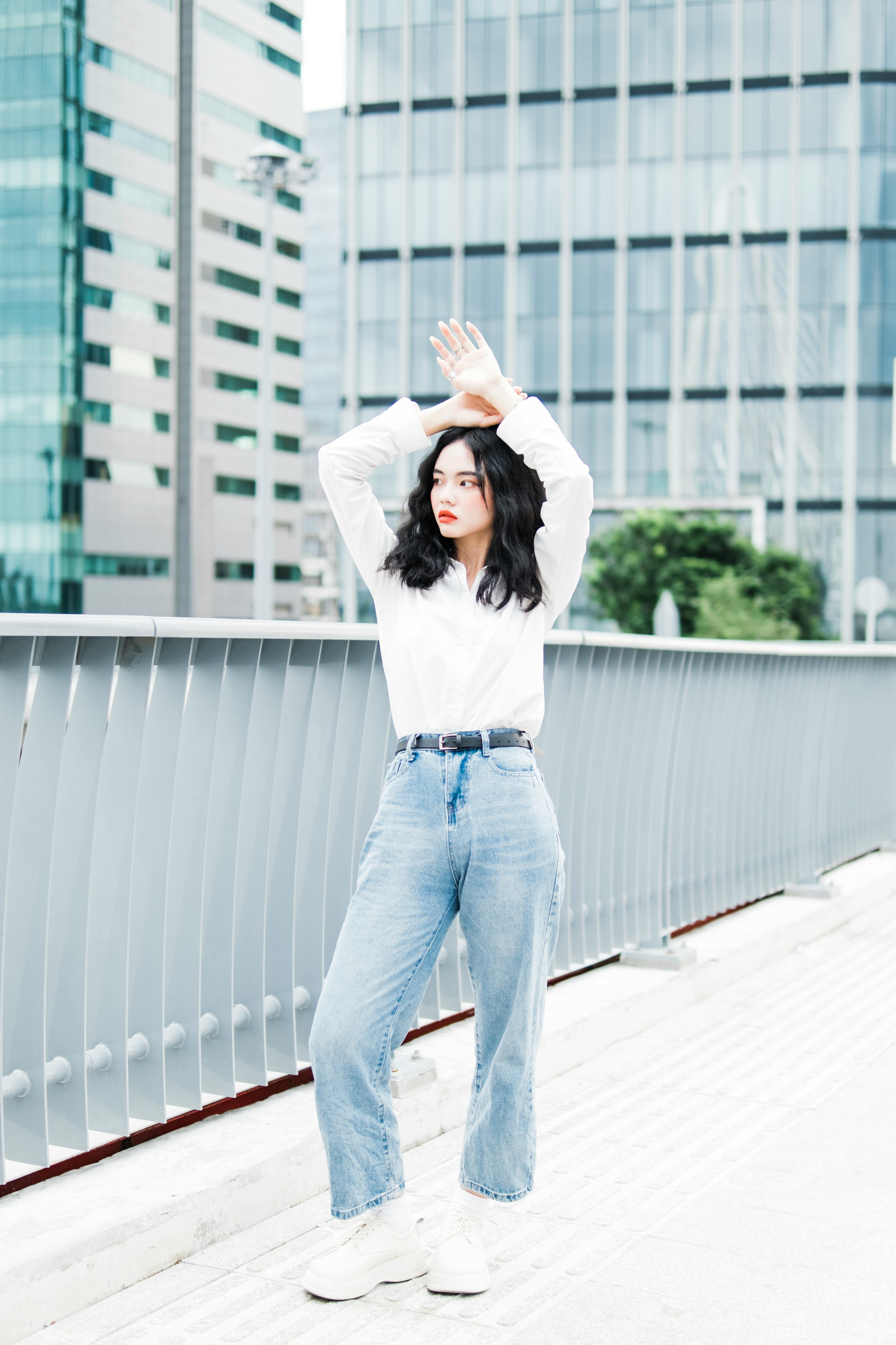 Stylish woman posing on a city bridge with modern buildings in the background.