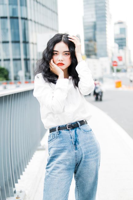 Fashionable woman with long black hair poses confidently in an urban cityscape.