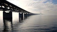 Grey Concrete Bridge on Body of Water Under Blue and White Sky during Daytime