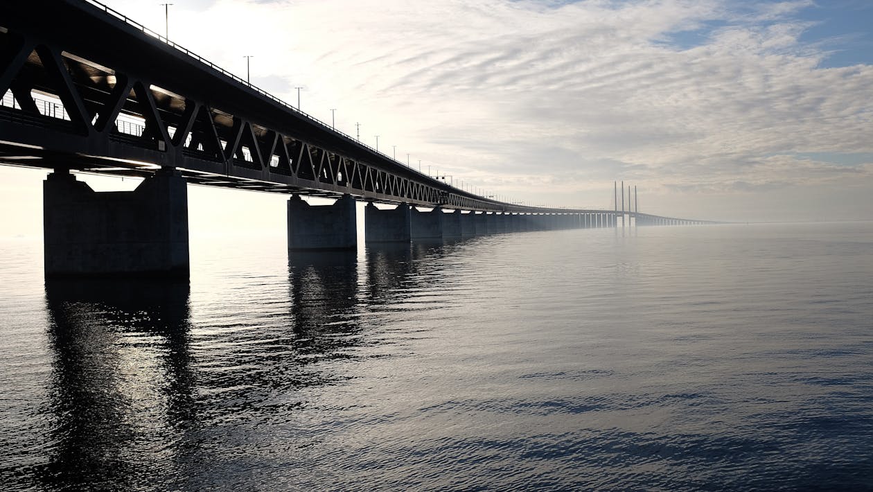 Free Grey Concrete Bridge on Body of Water Under Blue and White Sky during Daytime Stock Photo