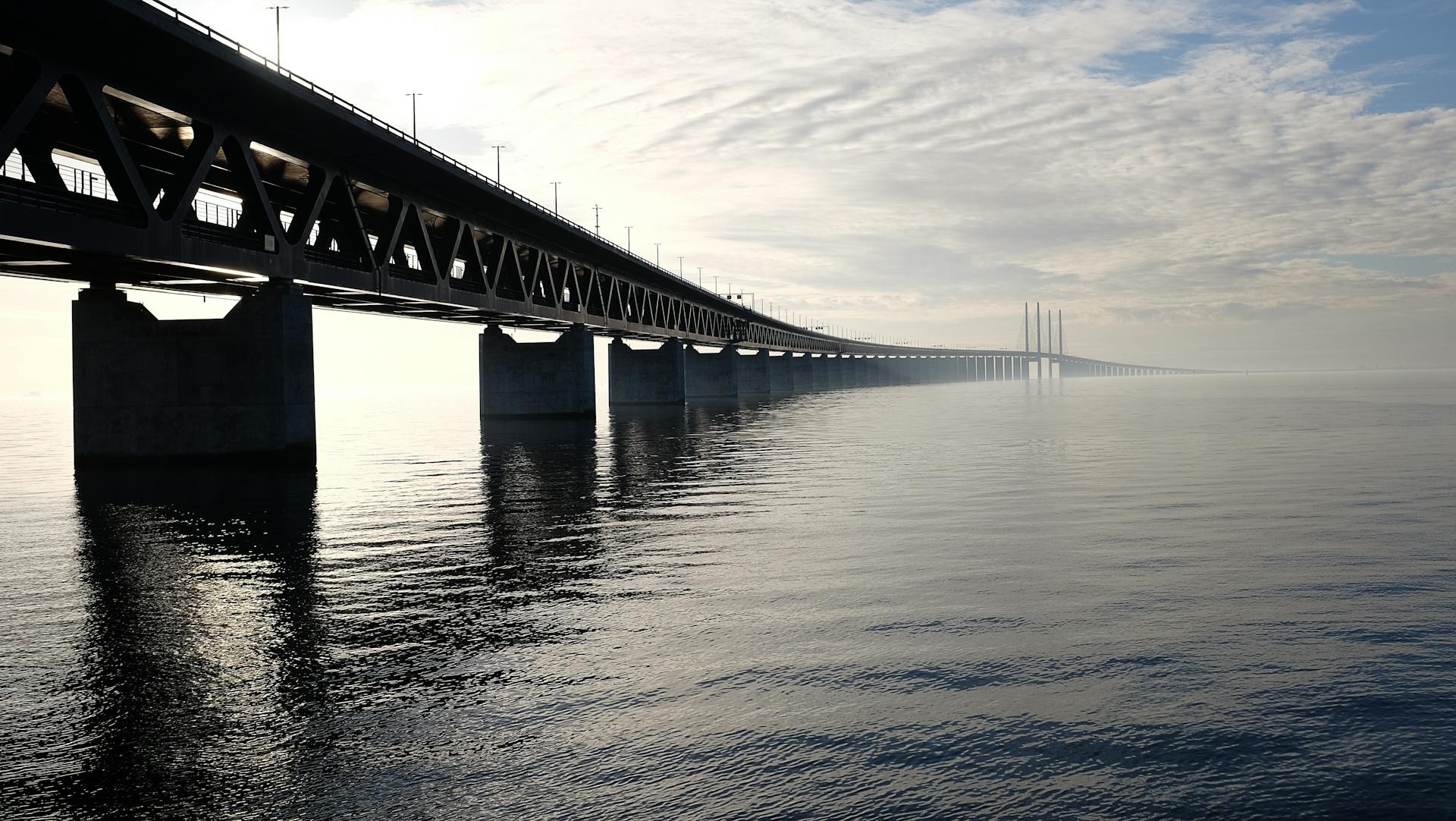 Grey Concrete Bridge on Body of Water Under Blue and White Sky during Daytime