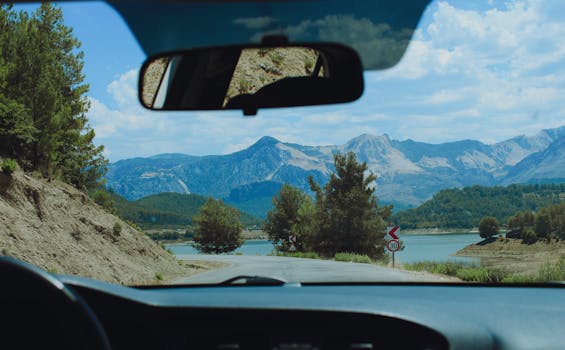 View from car interior of a winding road and mountain range with lush scenery, ideal for travel inspiration.