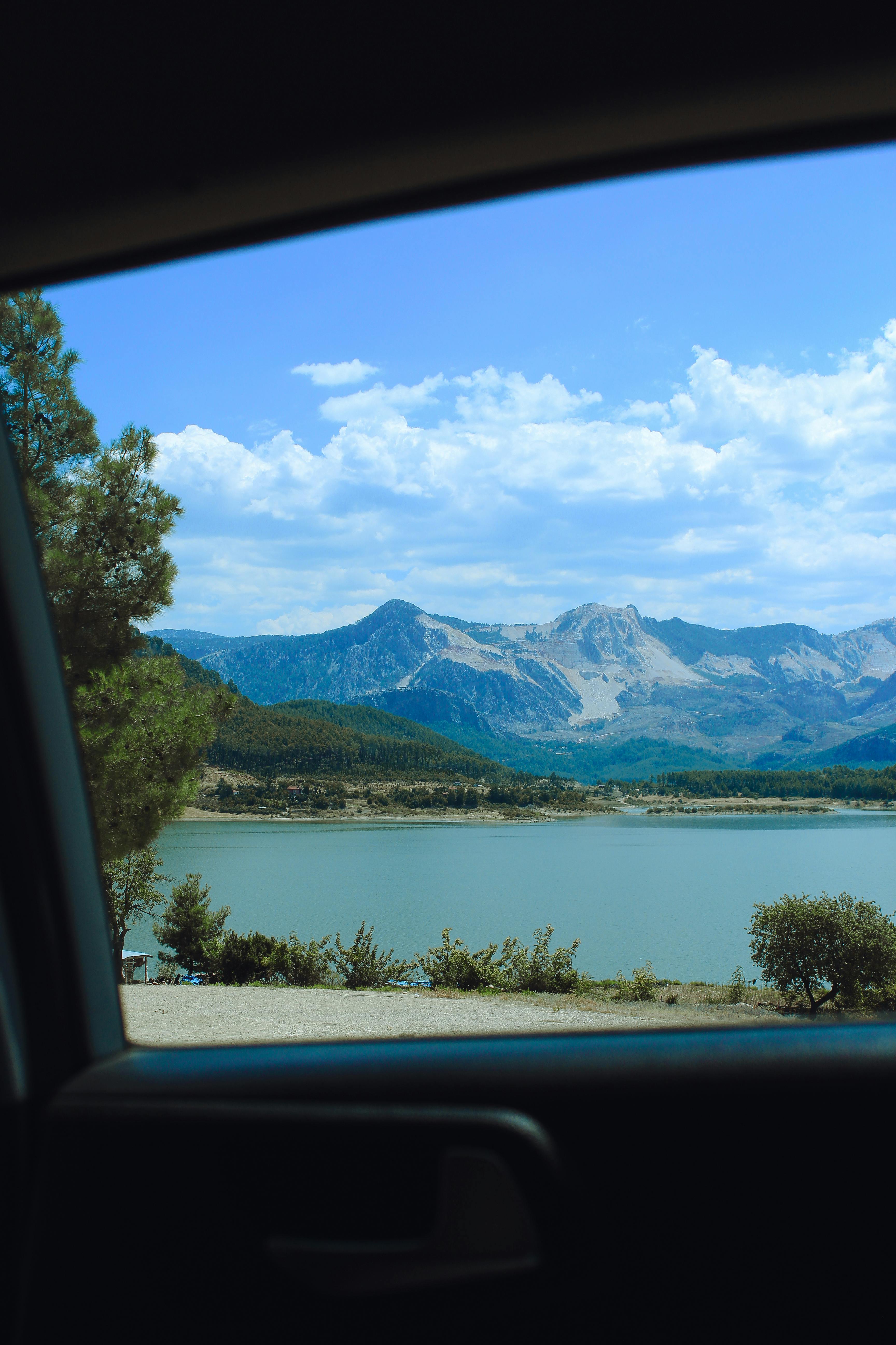 Serene view of mountains, lake, and blue sky captured from inside a car