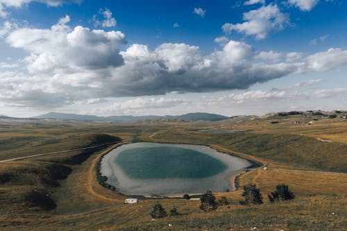 An Aerial Photography of a Lake Between Grass Field Under the Blue Sky and White Clouds