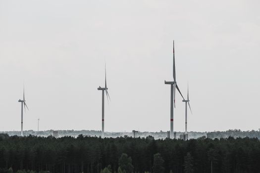 Wind turbines stand tall over a lush forest in Flanders, Belgium, showcasing renewable energy.