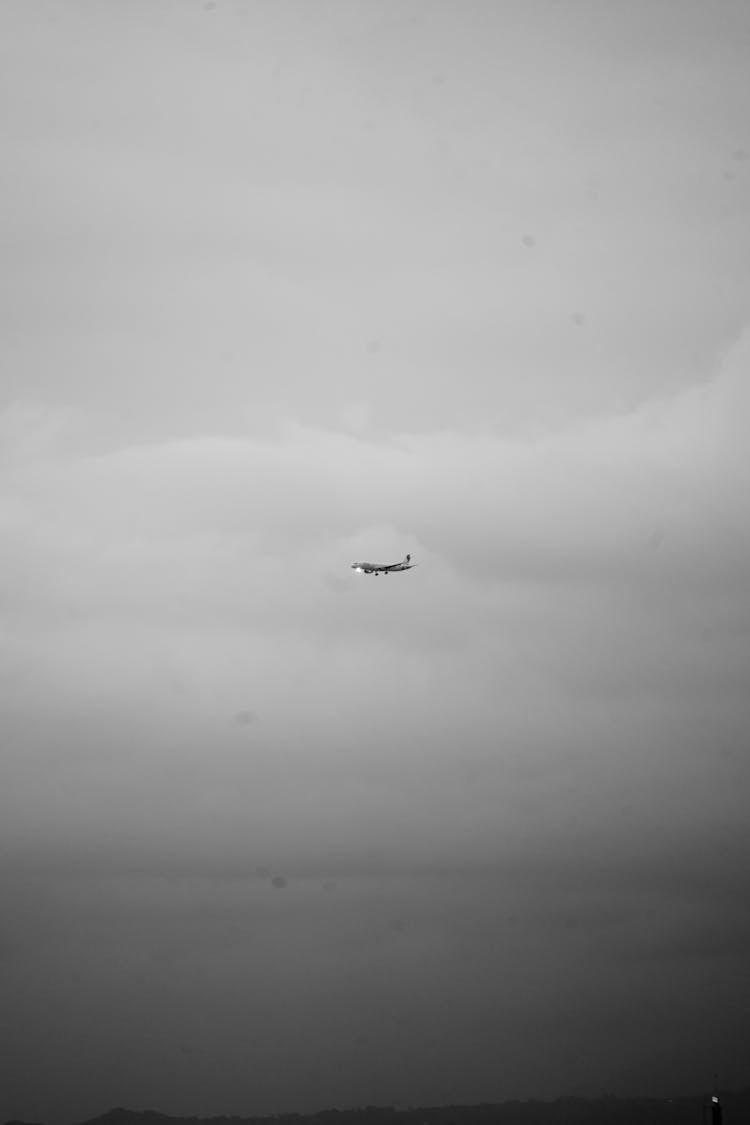 A Grayscale Photo Of An Airplane In Flight Near The Clouds