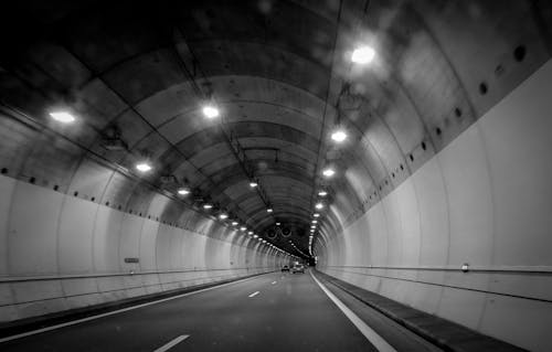 A Grayscale Photo of a Moving Cars Under the Tunnel With Lights