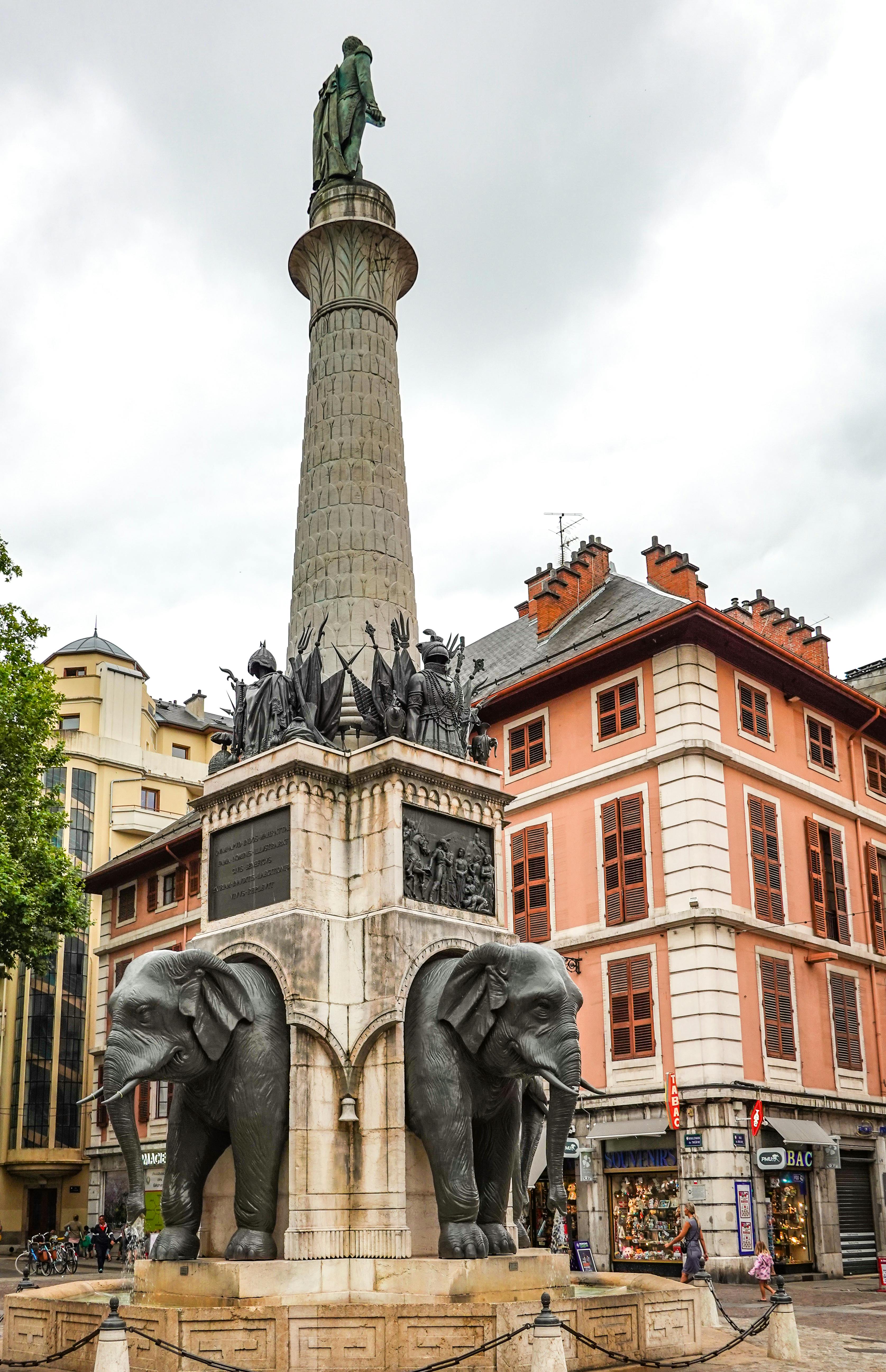 a low angle shot of a monument with elephants near the city buildings