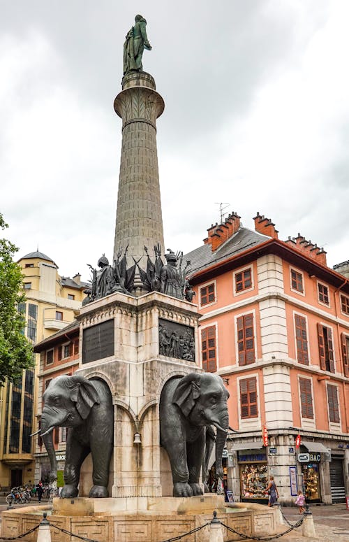 A Low Angle Shot of a Monument with Elephants Near the City Buildings