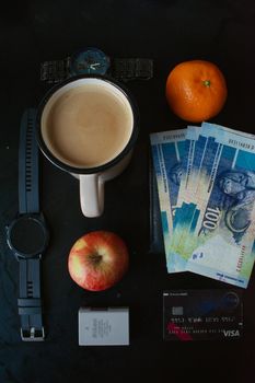 A flat lay with coffee, fruits, watches, cash, and credit card.