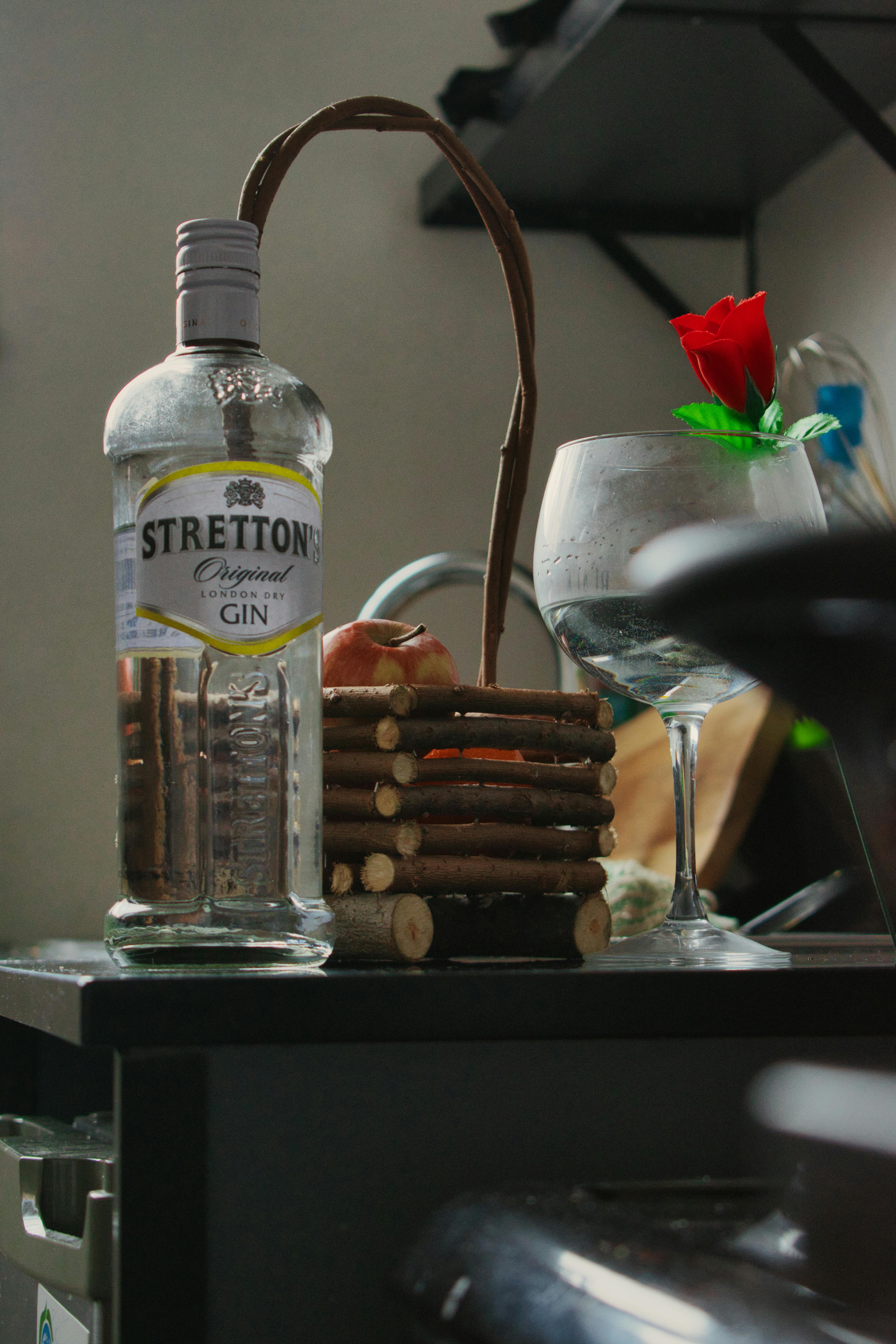 A detailed view of a Stretton Original Gin bottle accompanied by a decorative glass with a red flower indoors.