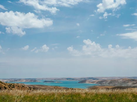 Captivating view of a tranquil lake surrounded by grasslands and clouds under a clear blue sky.