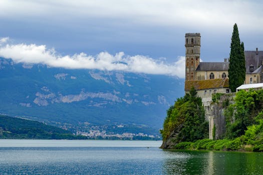Hautecombe Abbey by Lake Bourget with mountains in the background, showcasing Gothic architecture.