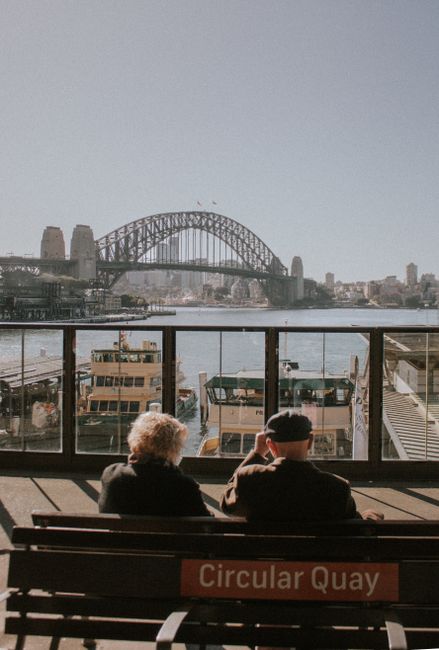 Senior couple seated at Circular Quay overlooking Sydney Harbour Bridge.