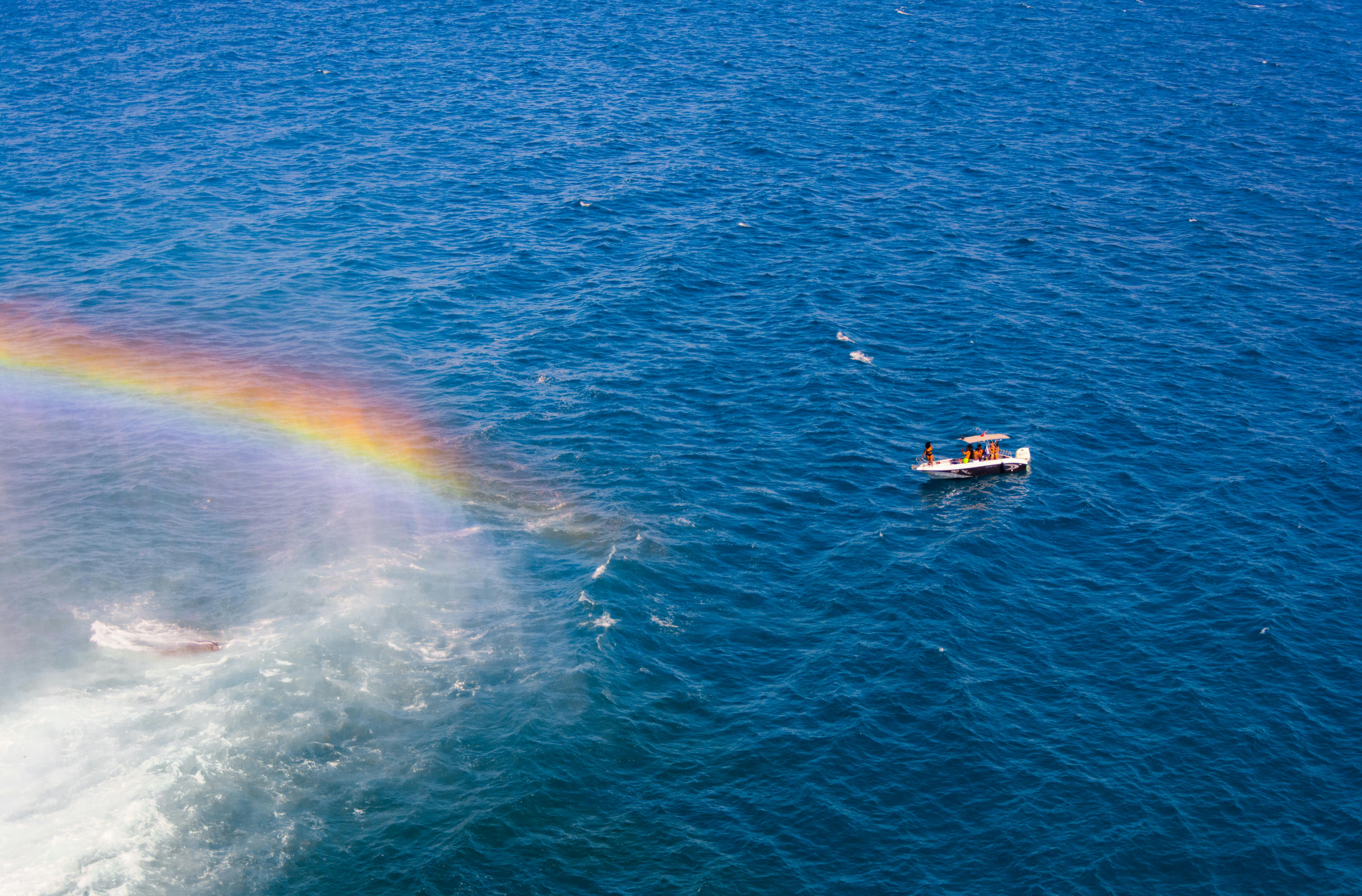 Stunning aerial view of a boat navigating the clear blue sea with a vibrant rainbow nearby, captured in Antalya, Türkiye.