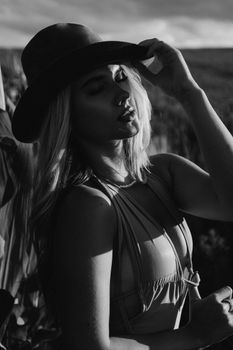 Elegantly dressed woman posing in sunlight, wearing a hat and swimsuit, offering a vintage fashion look.