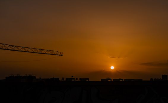 A crane silhouetted against a vibrant sunset sky over a city skyline, creating a dramatic urban scene.