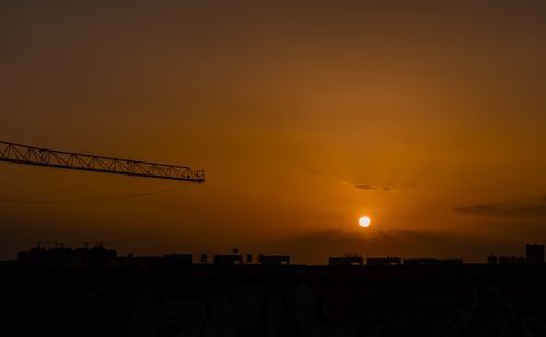 Free A crane silhouetted against a vibrant sunset sky over a city skyline, creating a dramatic urban scene. Stock Photo