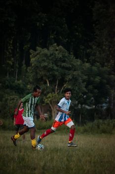 Teens playing a competitive soccer match outdoors on a grassy field during the day.