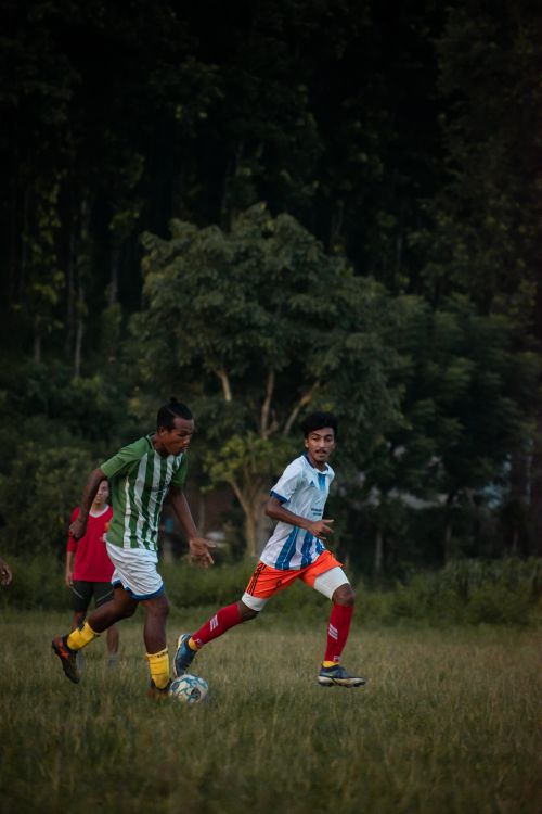 Free Teens playing a competitive soccer match outdoors on a grassy field during the day. Stock Photo