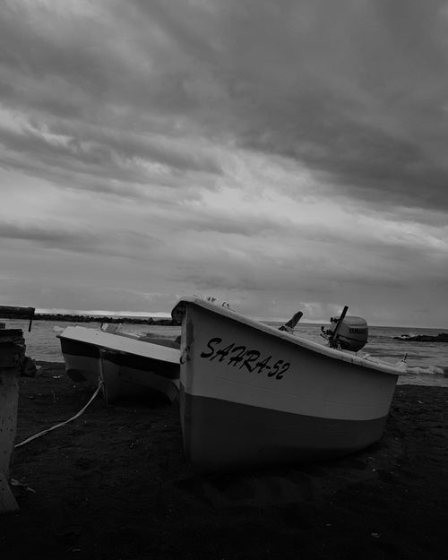 Free A tranquil grayscale scene of wooden boats docked on a quiet beach under a dramatic cloudy sky. Stock Photo