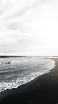 Peaceful beach scene with gentle waves crashing onto the shore under a cloudy sky.