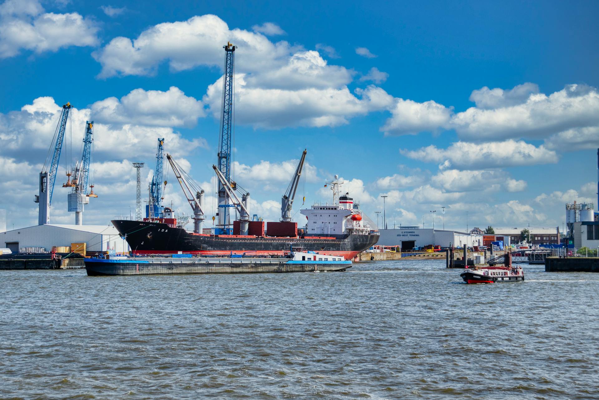 A busy harbor with cargo ships, cranes, and clear skies, showcasing maritime logistics.
