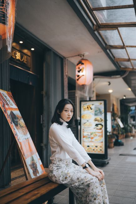 A fashionable Asian woman posing in a modern urban street with restaurant signs in the background.