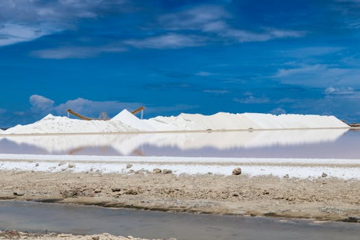 Aerial view of white salt piles under clear blue sky with reflecting water.