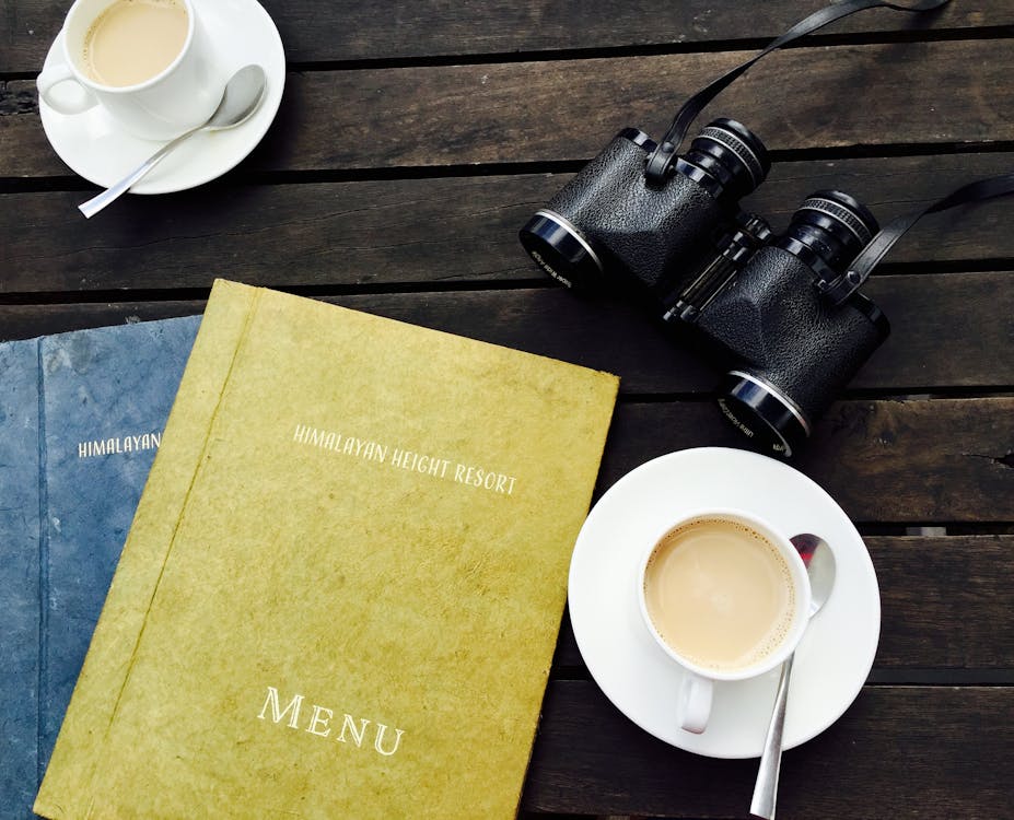 White Ceramic Tea Cup on White Saucer Near Menu Book 