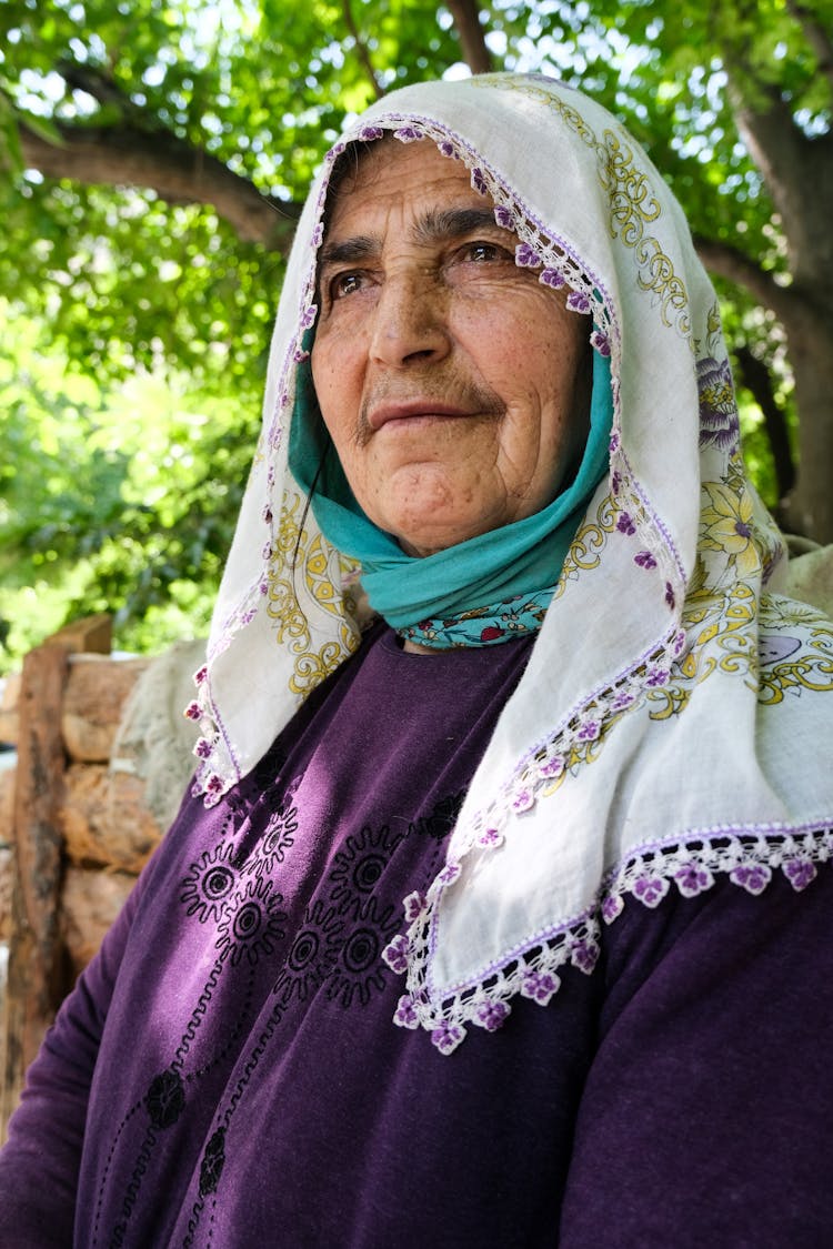 Man Standing In White Embroidered Headscarf And Purple Clothes