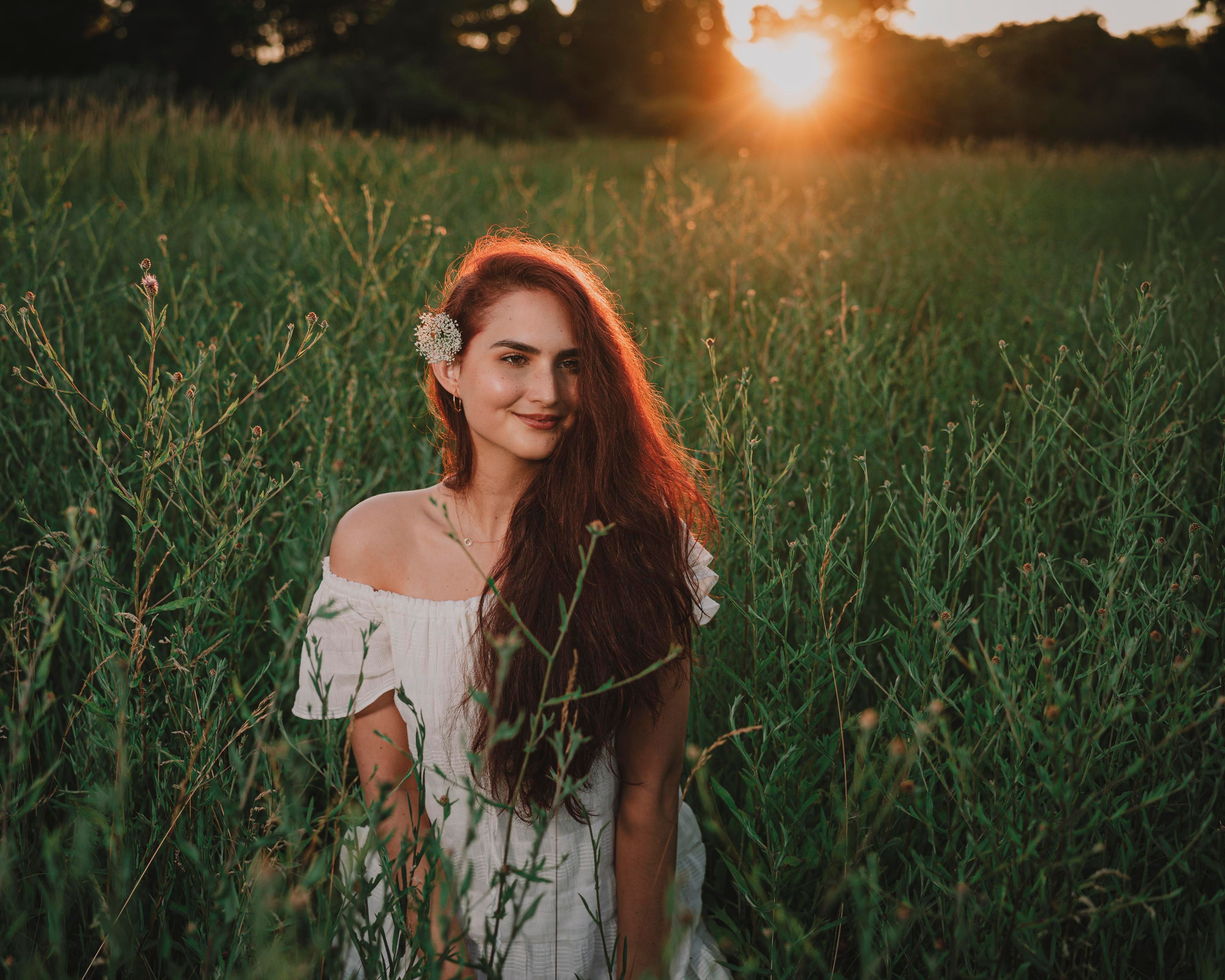 A woman in a white dress enjoying the serene beauty of a field at sunset, capturing a sense of peace and nature's charm.