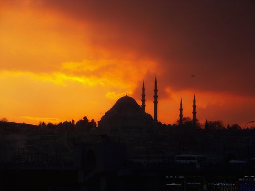 Free Dramatic silhouette of a mosque and its minarets against a vibrant orange sunset sky. Stock Photo