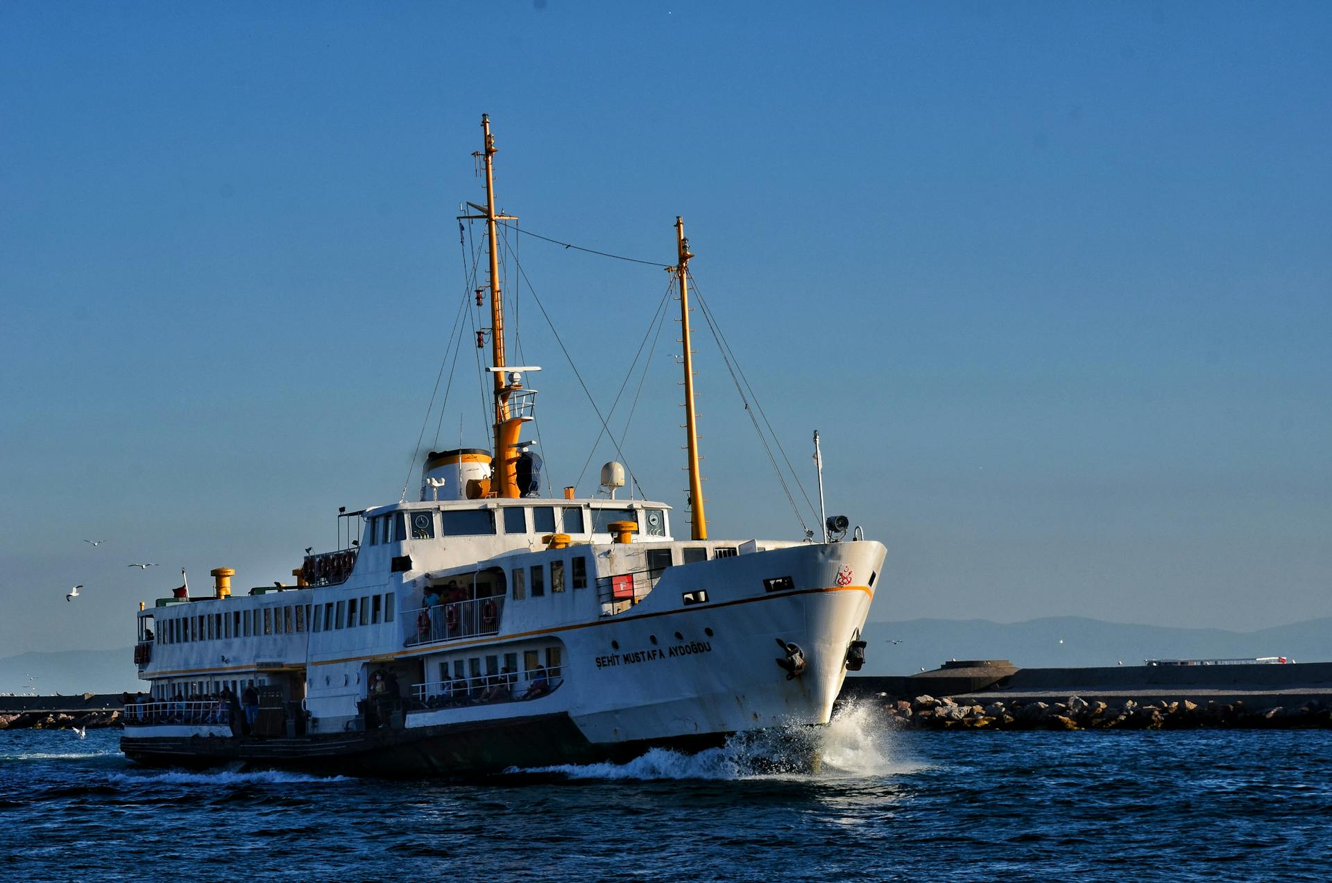 A passenger ferry vessel travels across a calm sea under a clear blue sky.