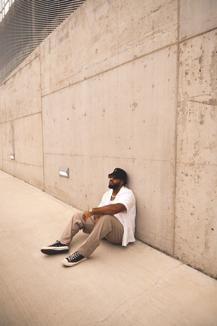 Man relaxing against a concrete wall in Gatineau, showcasing urban fashion.