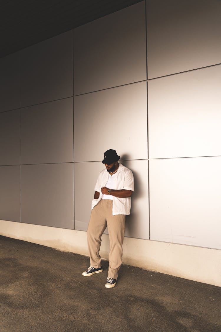 A Man In White Button Down Polo Leaning On The Wall While Looking Down